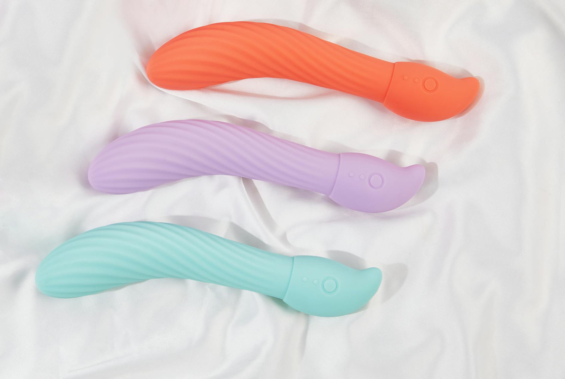 Colorful vibrators arranged on white fabric, highlighting their smooth texture