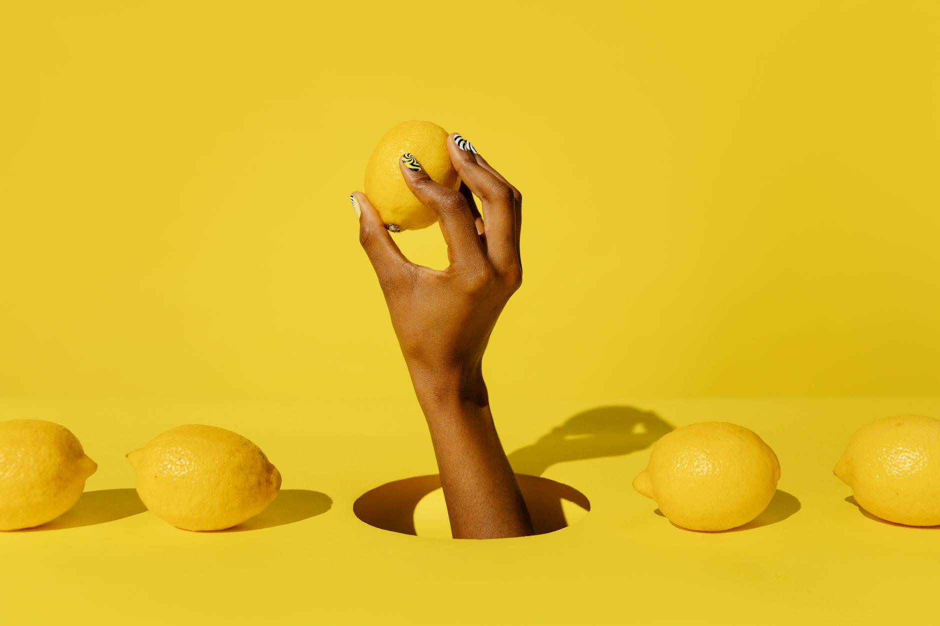 Hand holding a fresh lemon against a bright yellow background, symbolizing renewal and vitality