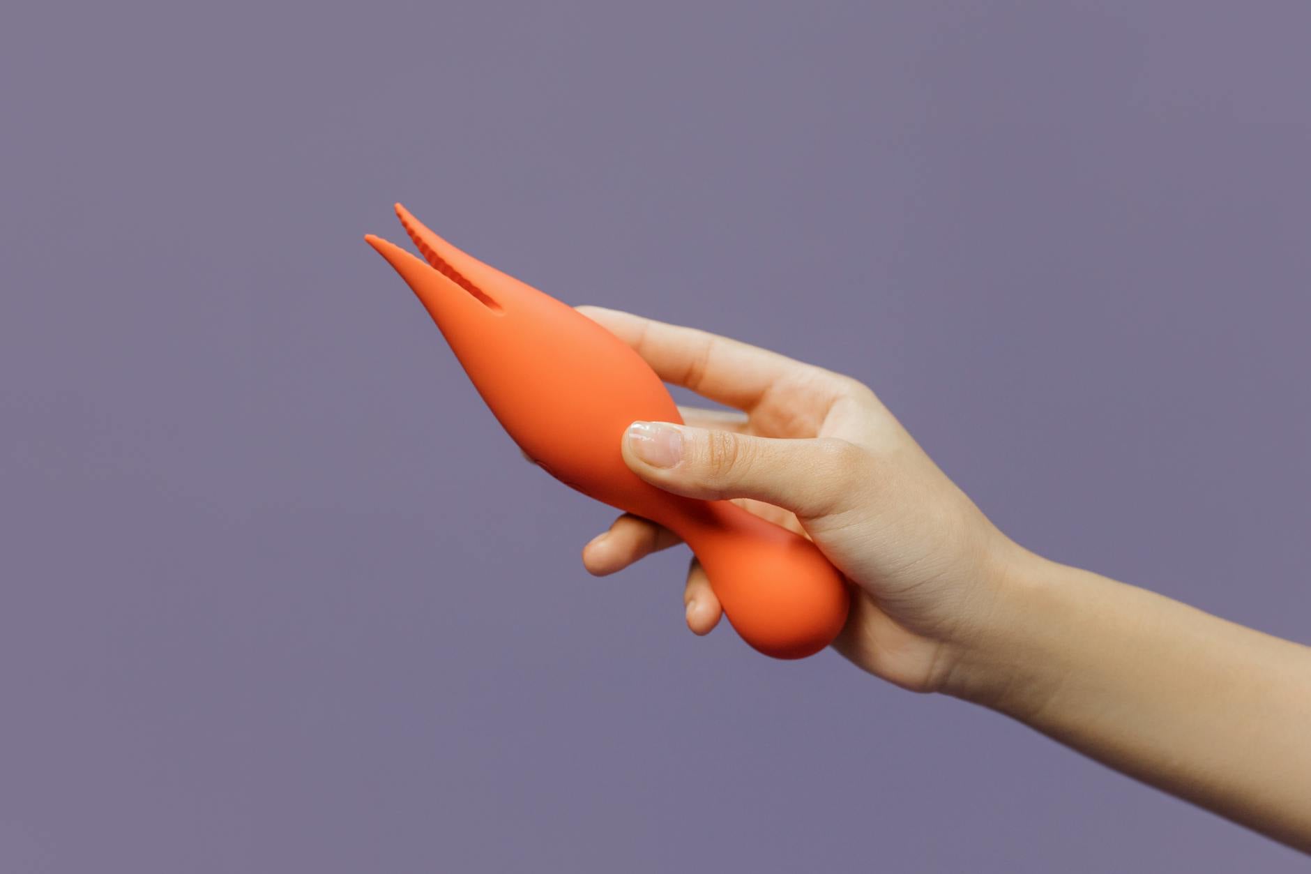 A hand holding a vibrator against a minimalistic backdrop, symbolizing couples exploring pleasure together without performance pressure.