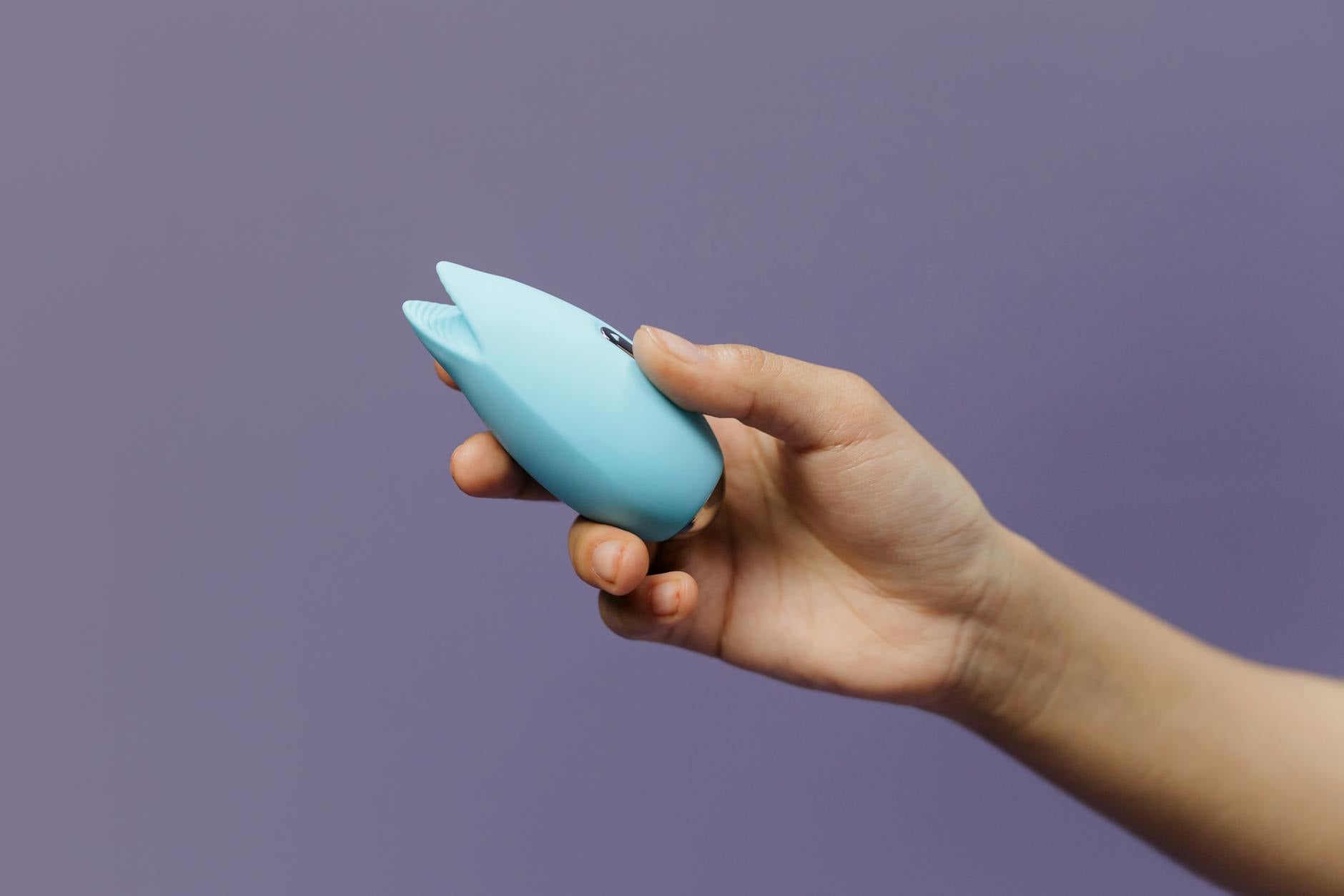 A blue silicone lemon vibrator held in hand against a purple background, demonstrating ergonomic design