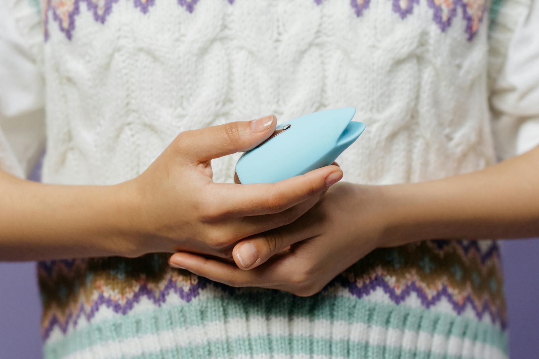 Close-up of hands holding a vibrator against a knitted sweater.
